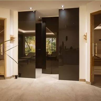 Ein moderner Wellnessbereich mit Zugang zu einer Infrarotkabine und einer Sauna. Die Atmosphäre ist entspannend und einladend, mit warmem Licht und Pflanzen.
