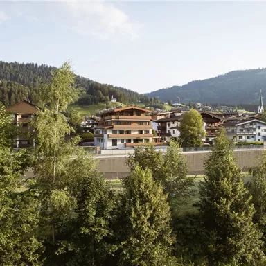 Eine malerische Landschaft mit traditionellen Häusern in den Bergen. Im Vordergrund sind viele Bäume und sanfte Hügel zu sehen.