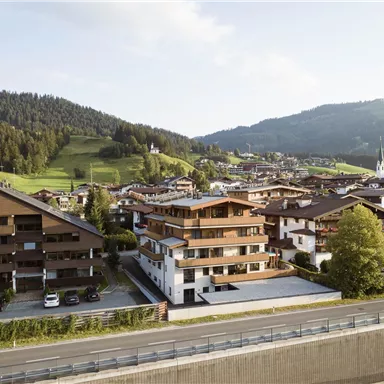 Eine malerische Aussicht auf ein Dorf mit modernen und traditionellen Gebäuden, umgeben von sanften Hügeln. Der Himmel ist klar und die Landschaft ist grün.