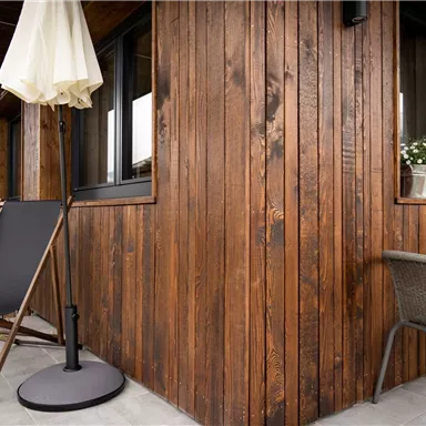 Ein gemütlicher Außenbereich mit hölzernen Wänden und einem kleinen Tisch. Zwei Liegestühle laden zum Entspannen ein.