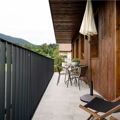 Ein gemütlicher Balkon mit Blick ins Grüne. Es gibt Holz- und Metallmöbel sowie einen Sonnenschirm.