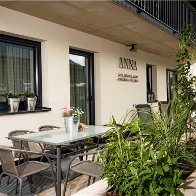 Ein gemütlicher Außenbereich mit einem Tisch und Stühlen. Pflanzen und Blumenkübel verleihen dem Raum eine einladende Atmosphäre.