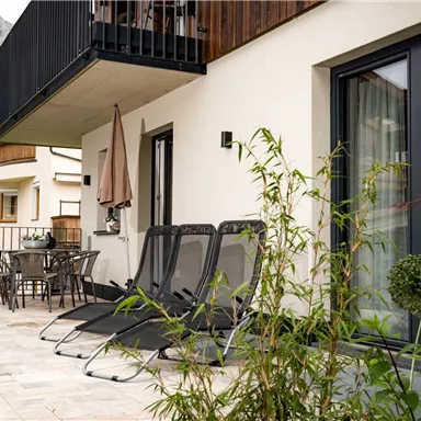 Eine moderne Terrasse mit Liegestühlen und einem Tisch. Im Hintergrund sind Berge und eine grüne Landschaft zu sehen.