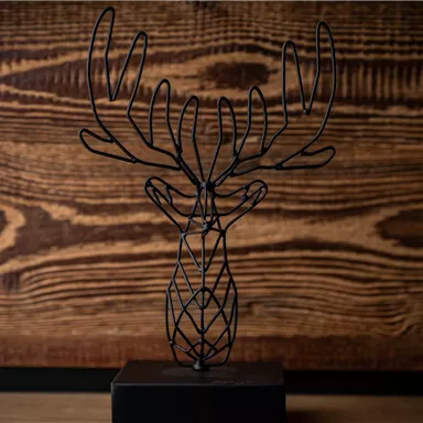Eine elegante Drahtskulptur eines Geweihs auf einem schwarzen Sockel. Der Hintergrund besteht aus Holz, was der Darstellung einen rustikalen Look verleiht.