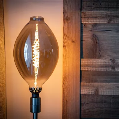 Eine stilvolle Lampe mit einer glühenden Glühbirne leuchtet sanft. Im Hintergrund ist eine Holzverkleidung zu sehen.
