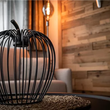 Eine moderne Obstschale in Form eines Apfels steht auf einem Tisch. Im Hintergrund sind eine gemütliche Couch und warme Lichtquellen zu sehen.