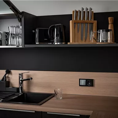 Eine moderne Küche mit einer schlichten Holzoberfläche. Auf den Regalen sind Gläser, eine Kaffeemaschine und ein Messerset zu sehen.