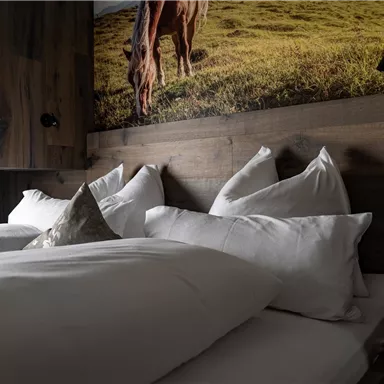 Ein gemütliches Schlafzimmer mit zwei Betten und Kissen auf weißen Bettbezügen. An der Wand ist ein Bild von einem Pferd auf einer Wiese.
