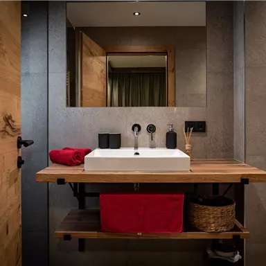 Ein modernes Badezimmer mit einem weißen Waschbecken auf einem Holzregal. Die Wände sind in neutralen Tönen gehalten, und es gibt einen großen Spiegel.