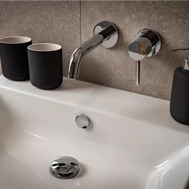 Ein modernes Waschbecken mit chromfarbenen Armaturen. Neben dem Waschbecken stehen schwarze Behälter und ein Seifenspender.