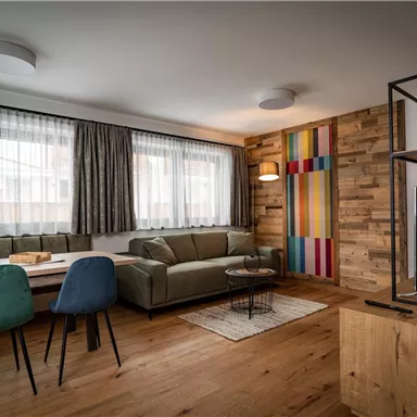 Ein modernes Wohnzimmer mit einer gemütlichen Couch und großen Fenstern. Die bunten Wände und der Holztisch verleihen dem Raum eine einladende Atmosphäre.