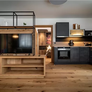 Eine moderne Wohnung mit einem offenen Küchenbereich und einem Wohnzimmer. Der Raum ist mit Holzfußboden und eleganten Möbeln ausgestattet.