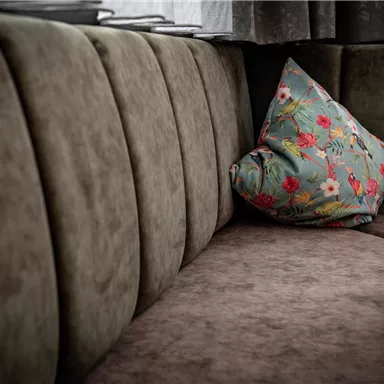 Eine gemütliche Sitzecke mit einem beigen Sofa und einem dekorativen Kissen. Das Kissen hat ein buntes Blumenmuster und sorgt für einen Hauch von Farbe.