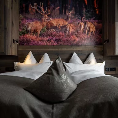 Ein gemütliches Schlafzimmer mit einem großen Bett und dekorativen Zierkissen. Im Hintergrund befindet sich ein eindrucksvolles Bild von Rehen in der Natur.
