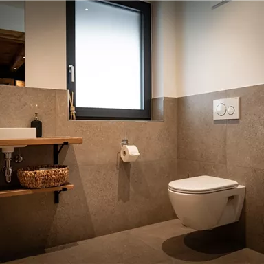 Ein modernes Badezimmer mit einem minimalistischen Design. Es enthält ein Waschbecken, eine Toilette und ein großes Fenster, das natürliches Licht hereinscheinen lässt.