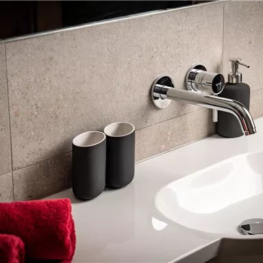 Ein modernes Waschbecken mit einem glänzenden Wasserhahn. Daneben stehen zwei schwarze Becher und frische Handtücher.