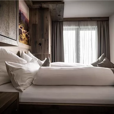 Ein modernes Schlafzimmer mit Holzverkleidung und einem gemütlichen Doppelbett. Das Fenster lässt sanftes Licht herein und sorgt für eine warme Atmosphäre.