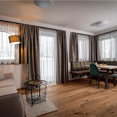 Ein modernes Wohnzimmer mit großen Fenstern und Vorhängen. Es enthält ein Sofa, einen Essbereich und einen Holzfußboden.