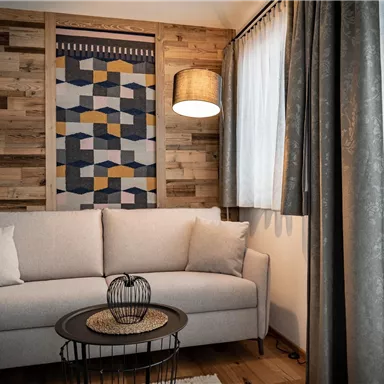 Ein modernes Wohnzimmer mit einem hellen Sofa und einem stilvollen Tisch. Die Wände sind mit Holzverkleidung und einem dekorativen Wandteppich gestaltet.