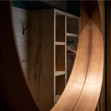 Ein stilvolles Innendesign mit einem großen Spiegel und einem offenen Kleiderschrank aus hellem Holz. Die Wände sind ebenfalls aus Holz, was eine warme Atmosphäre schafft.