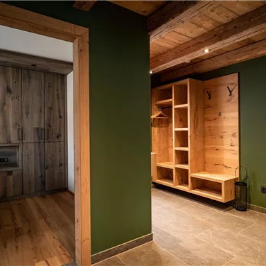 Ein moderner Eingangsbereich mit Holzdetails und grünen Wänden. Auf der linken Seite befindet sich ein Schlafzimmer und auf der rechten Seite ein offenes Regal.