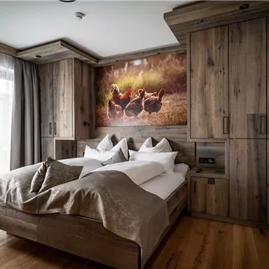 Ein gemütliches Zimmer mit Holzmöbeln und zwei Betten. An der Wand hängt ein Bild von Hühnern in der Natur.