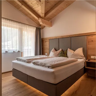 Ein gemütliches Schlafzimmer mit einem großen Bett und Holzelementen. Helle Fenster sorgen für eine freundliche Atmosphäre.