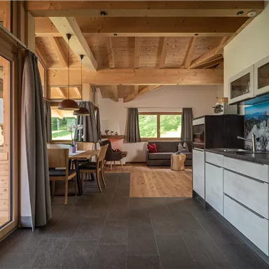 Eine moderne Küche mit Holzdecken und großen Fenstern. Der Raum ist offen und hell, mit einem Essbereich und einem gemütlichen Wohnzimmer.