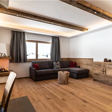 Ein gemütliches Wohnzimmer mit einem modernen Sofa und Holzfußboden. Die Fenster sind mit Vorhängen geschmückt, und ein Kamin sorgt für eine angenehme Atmosphäre.