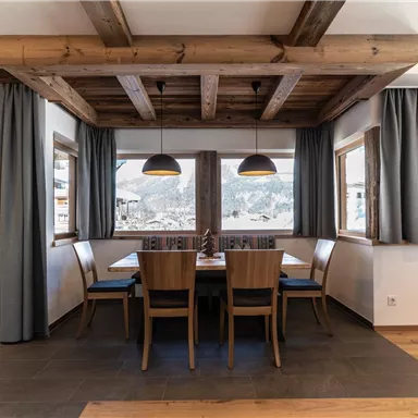 Ein modernes Esszimmer mit Holzdecken und großen Fenstern. Es gibt einen Tisch mit Stühlen und eine helle, einladende Atmosphäre.