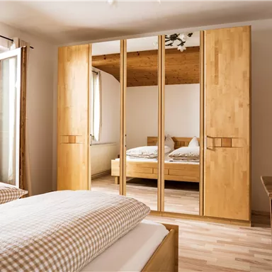 Ein helles Schlafzimmer mit einem großen Spiegelkleiderschrank. Das Zimmer ist modern eingerichtet und hat ein großes Fenster mit Blick ins Grüne.