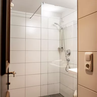 Ein modernes Badezimmer mit einer Glasdusche. Die Wände sind mit weißen Fliesen gestaltet und der Boden ist in einem dunklen Grauton.