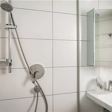 Eine moderne Dusche mit einer klaren Duschkabine und einem Waschbecken. Die Wände sind mit fliesenartigen weißen Fliesen verkleidet.