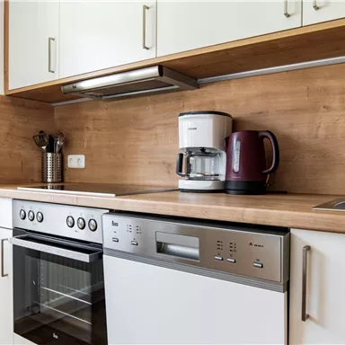 Eine moderne Küche mit einer Holzarbeitsplatte und weißen Schränken. Auf der Arbeitsfläche stehen eine Kaffeemaschine und ein Wasserkocher.