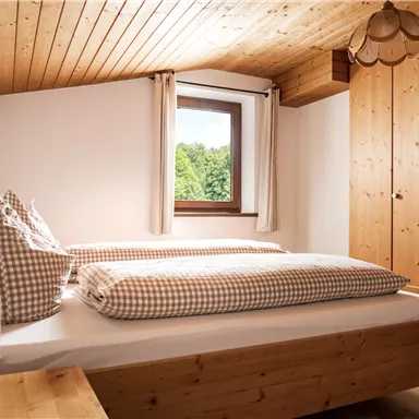 Ein helles Schlafzimmer mit Holzdecken und Wänden. Das Zimmer hat ein Fenster mit Blick ins Grüne und eine gemütliche Bettausstattung.