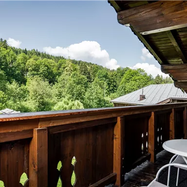 Ein schöner Balkon mit Holzelementen und Blick auf grüne Wälder. Der Himmel ist klar und die Sonne scheint.