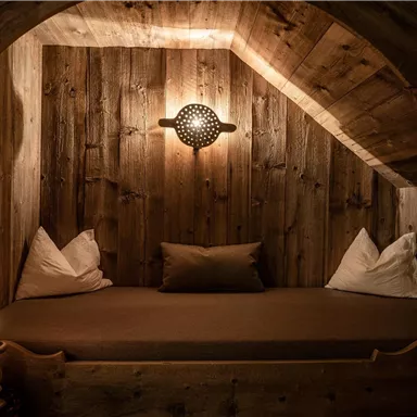 A cozy corner with a wooden bed and pillows. Soft light and warm wooden walls create a relaxing atmosphere.