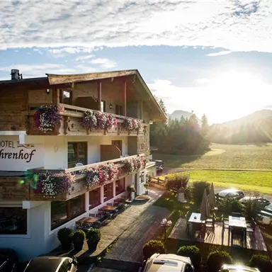 A charming country hotel with blossoming balcony plants and a picturesque landscape in the background. The sun rises and illuminates the surroundings.