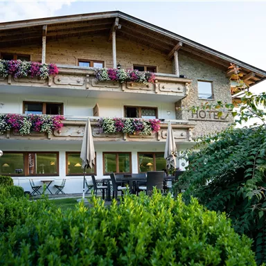 A charming hotel building with wooden balconies, adorned with colorful flowers. The garden is green and inviting, ideal for outdoor relaxation.