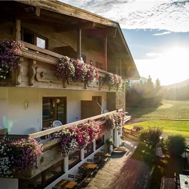 A charming hotel with blooming balcony plants and a picturesque view of the landscape. The sun rises and bathes the scene in warm light.
