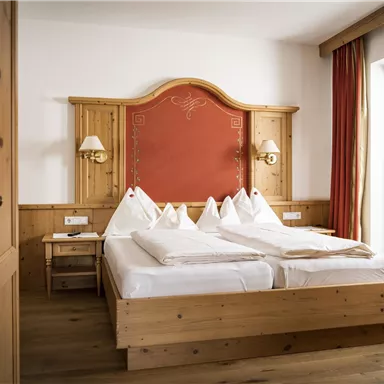 A cozy bedroom with a large double bed and wooden interiors. The room features a window with a view outside and warm colors.