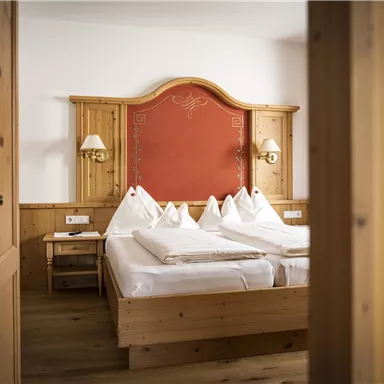 A cozy bedroom with a large wooden bed and red accents. The warm wood materials create an inviting atmosphere.