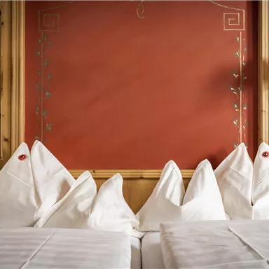 A cozy bedroom with wood decor and a red wall. On the bed lie several decorative pillows in elegant shapes.