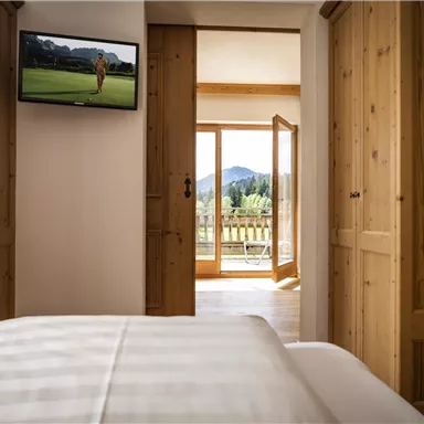 A cozy room with wooden details and a television. The open door offers a view of a beautiful landscape with mountains.