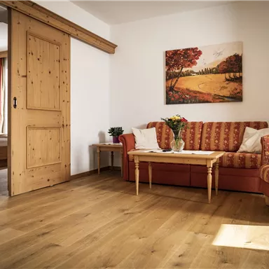 A bright living room with a red sofa and a small table. On the wall hangs a picture of an autumn landscape.