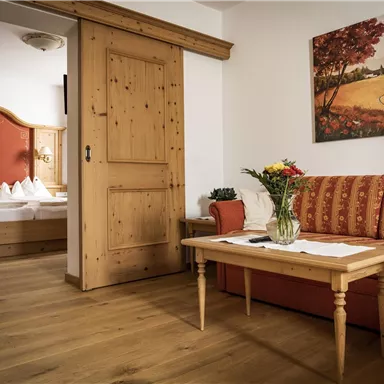 A cozy room with wooden decor and a red sofa. In the background, another bedroom is visible, decorated in warm colors.