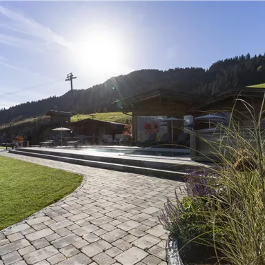 A beautiful landscape with a paved terrace and a pool. In the background, you can see a sunny sky and wooded hills.