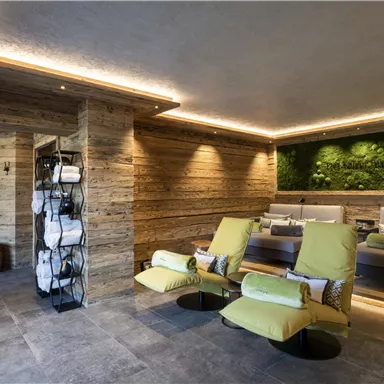 An elegant relaxation room with comfortable loungers and wooden paneling. The green plant wall creates a soothing atmosphere.