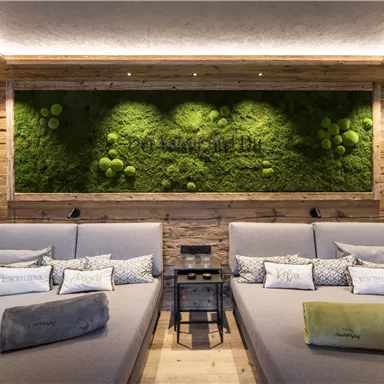 A stylish wellness room with two cozy loungers. The wood paneling and the green moss wall create a relaxing atmosphere.