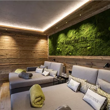 A stylish wellness room with cozy loungers and a green moss wall. The warm wood elements create a relaxed atmosphere.
